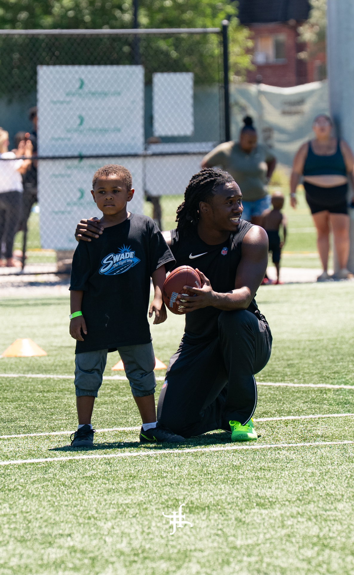 Pro athlete kneeling with a young camper on the field